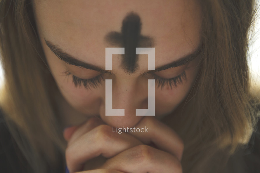 cross of ashes on a woman's forehead as she prays on Ash Wednesday 