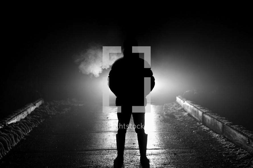 silhouette of a man standing in darkness and smoke 