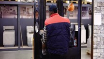 Forklift operator in the warehouse, wearing uniform and cap.