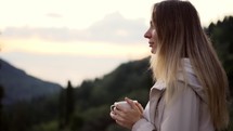Blonde woman admiring view of the mountains sipping a drink.