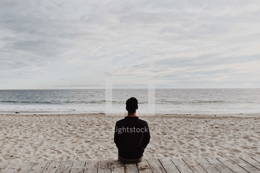 a man sitting on a boardwalk on a beach 
