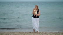 Mother cuddling baby, scene at the beach against the sea
