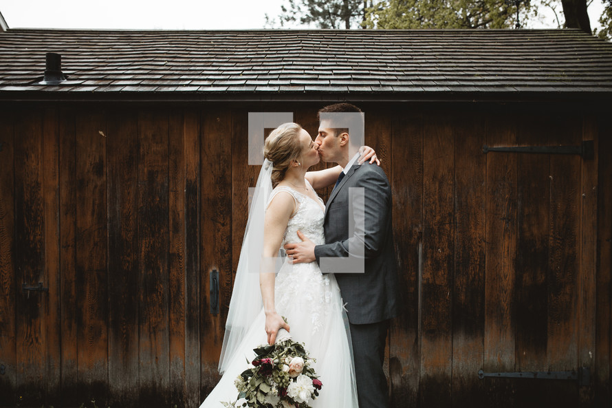 bride and groom kissing in front of a barn 