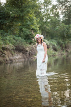 a woman in a white dress with flowers in her hair walking in water 