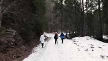 Tourists Trekking On Snow-Covered Dirt Road In Forest Woods During Winter. Dolly Shot