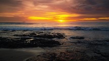 Glowing and colorful sun setting over ocean with waves crashing on shore