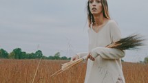 a woman walking through a field carrying a sheath of wheat 