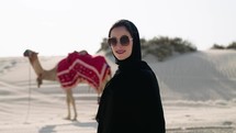 Portrait of Muslim woman at the desert with camel behind
