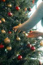 Womans hand decorating a Chrstmas tree with baubles