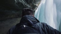 a man walking through a cave and looking at a frozen waterfall 