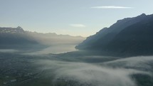 Aerial drone flying through the misty mountains with small chalet and homes below
