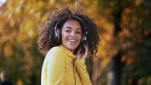Girl's face in headphones. Young woman in yellow enjoys music while sitting in park.