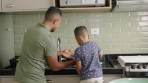 Son helping dad to clean the dishes, washing utensils together, household chores