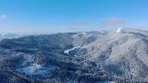 Scenic View Of Snowy Mountains With Pine Trees Against Blue Cloudy Sky - aerial drone shot