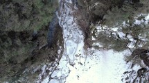 Drone Descending On Narrow River Flowing On Towering Rock Mountains During Winter. Aerial Shot