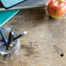 teal and gray books with pens on desk with apple 