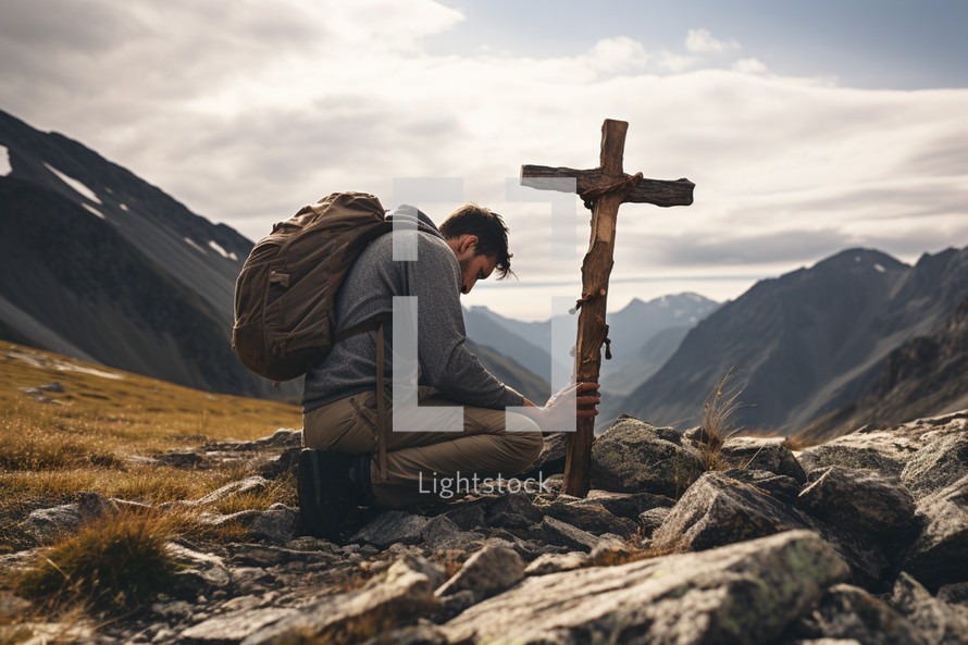 Young Hiker Prays at a Cross in the Mountains
