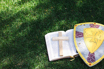 cross on bible with shield in grass