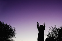 silhouette of a child with raised hands at sunset 