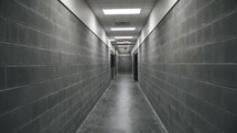 Camera moves through prison facility hallway with stone walls.
