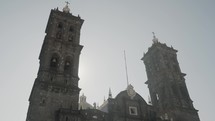 Beautiful historic large cathedral Basilica de Puebla in Mexico where the sun comes out behind one of the church towers on a summer day. Wide trucking shot