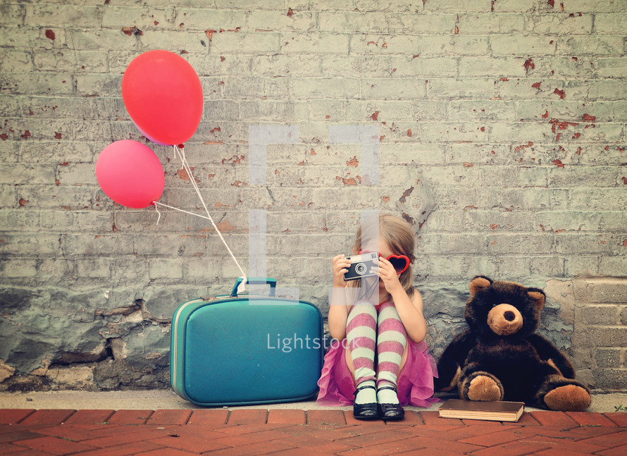 a little girl sitting with balloons and luggage 