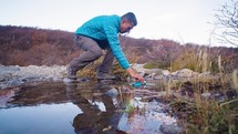 Male traveler drinks clean water from river or spring in autumn forest. Female tourist with backpack drinking fresh mountain water while a hiking, scooped up cold transparent water with his
