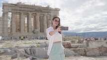 A tourist woman on summer vacations taking selfie at the Parthenon Temple at the Acropolis of Athens, Greece