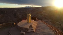 Aerial shot drone orbits monument at viewpoint overlooking San Pedro, Death Valley, and the red desert mountains in Atacama with a brilliant sunset in a medium shot