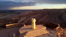 Aerial shot drone orbits monument at viewpoint overlooking San Pedro, Death Valley, and the red desert mountains in Atacama with a brilliant sunset