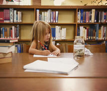 a child in a library doing homework next to a jar for education funds 
