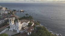 Drone flies to the right of Santo Antonio da Barra Church as it heads to the beach at sunset in Salvador, Bahia, Brazil