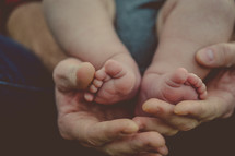 Infant's feet in a parent's hands.