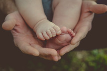 Infant's feet in a parent's hands.