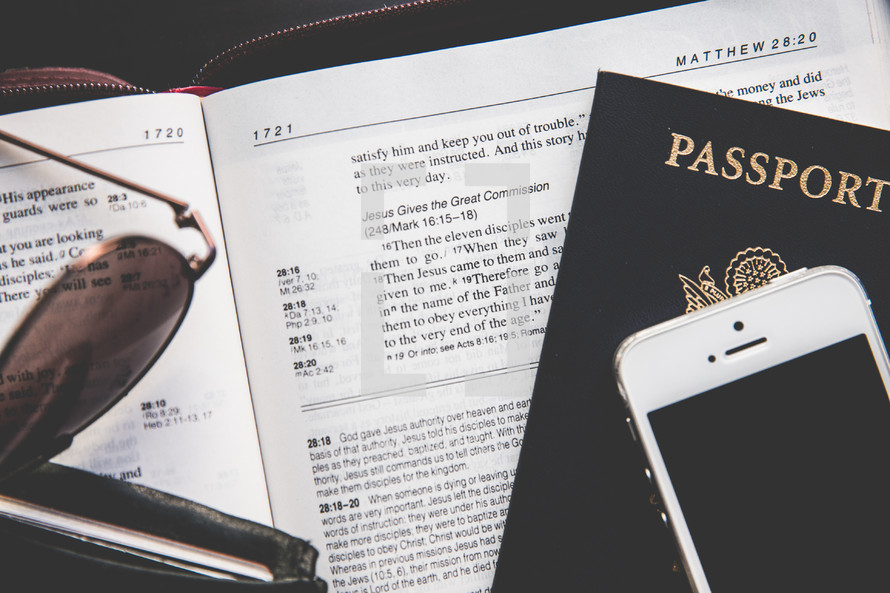 Bible, wallet, passport, sunglasses, and iPhone on a table 