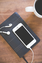 iphone and earbuds on a Bible and a coffee mug 