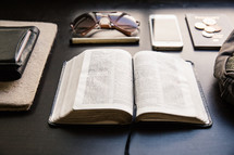 Bible, wallet, passport, sunglasses, pen, iPhone, and journal on a table 