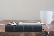 an iPhone and earbuds on a Bible and a coffee mug