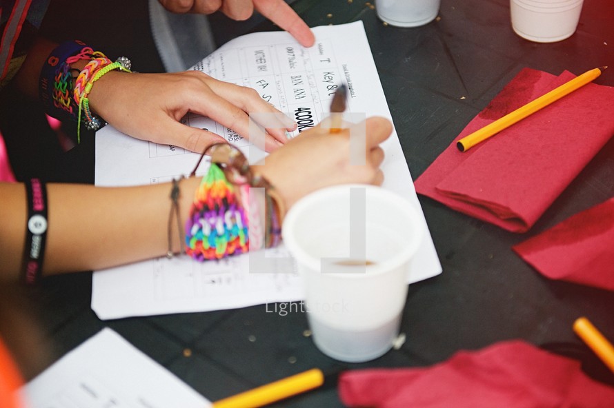 A woman wearing many colored yarn bracelets fills out a form at a table.