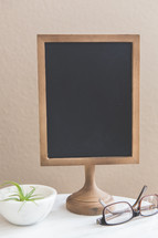 chalkboard on a stand, houseplant, and reading glasses 