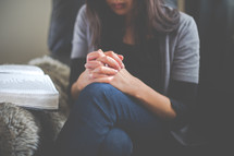 a woman praying near an open Bible 