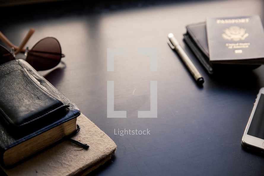 Bible, wallet, passport, sunglasses, pen, iPhone, and journal on a table 