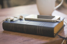 iphone and earbuds on a Bible and a coffee mug 