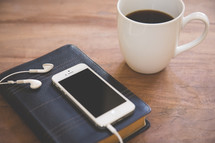iPhone and earbuds on a Bible and a coffee mug 