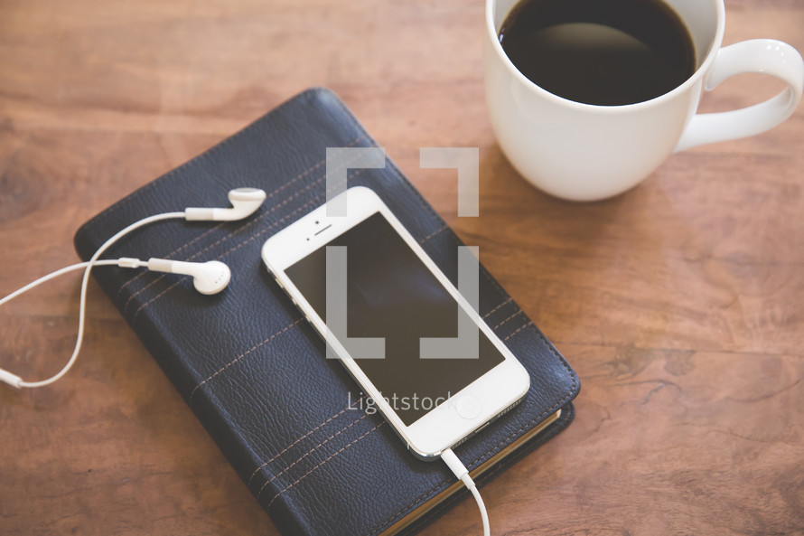 on iPhone and earbuds on a Bible and a coffee mug