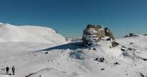 Aerial, drone shot towards people at the sphinx rock formation, on the top of the southern Carpathians, on a sunny winter day, in the Bucegi Natural Park, Romania
