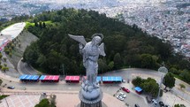 Aerial shot drone flies down and backwards while panning the camera from above Panecillo, the virgin statue on the hill overlooking the city Quito