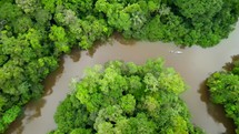 Aerial shot drone flying to right with camera pointing down following canoe full of people paddling down brown river in middle of Amazon rainforest