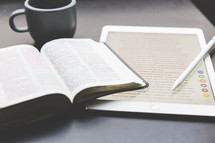 An open Bible, an electronic tablet, and a cup of coffee.