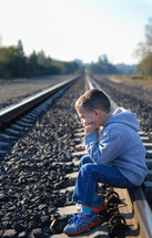 boy child sitting alone on railroad tracks 